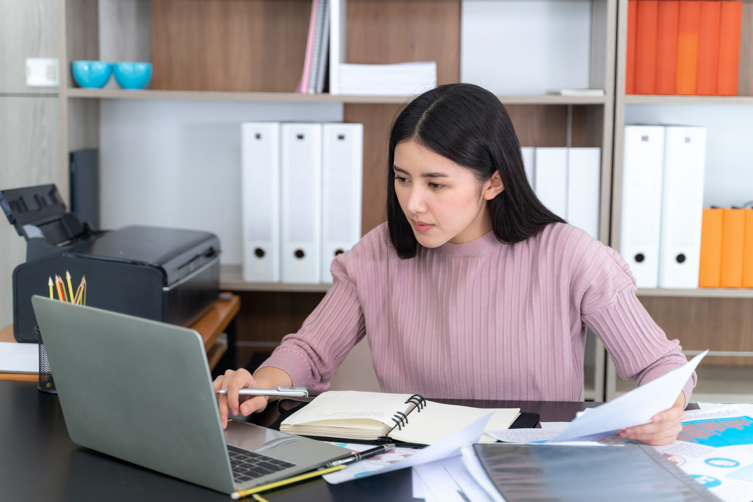 Young pretty woman working with laptop computer on table in the office, She checking paperwork together